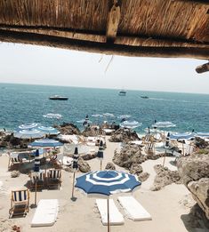 chairs and umbrellas on the beach with boats in the water