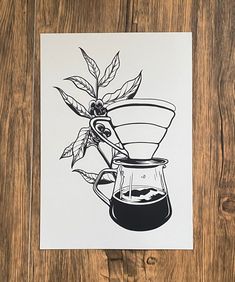 a black and white drawing of a coffee pot with leaves on it, next to a wooden table