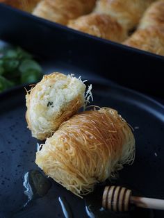 two croissants on a black plate with honey and greens in the background