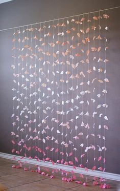 some pink and white paper flowers hanging from the ceiling in front of a gray wall