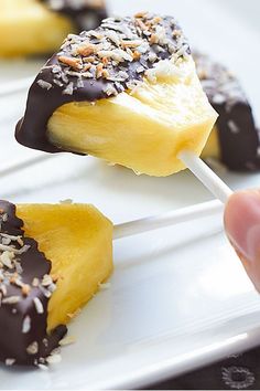 a hand holding a banana on a stick with chocolate and sprinkled toppings