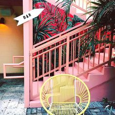 a yellow chair sitting in front of a pink building with palm trees on the balcony