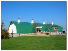 a large green and white barn sitting on top of a lush green field