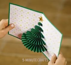 someone is holding up a folded card with green paper trees on it and gold stars