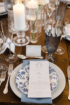 the table is set with white and blue plates, silverware, candles and napkins