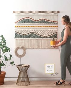 a woman standing in front of a wall hanging with a potted plant on it