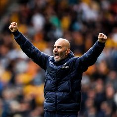 a bald man with his arms in the air and one hand raised up as he stands on a soccer field