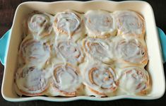 a pan filled with cinnamon rolls sitting on top of a wooden table next to a blue dish