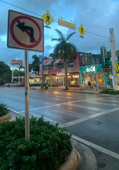 an intersection with several street signs and palm trees in the background at dusk, on a cloudy day