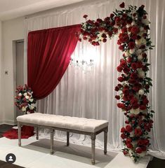 a white bench sitting under a red and white drape with flowers on the wall