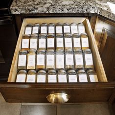 a drawer full of jars with labels on them sitting on a marble counter top next to an oven