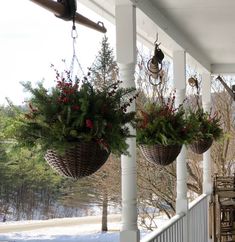 three hanging baskets filled with plants on a porch next to trees and snow covered ground