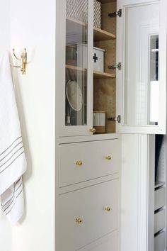 a white cabinet with glass doors and drawers next to a towel rack in a bathroom