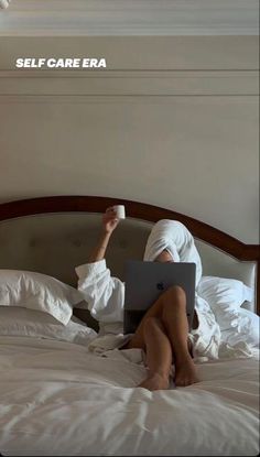 a woman laying in bed with her legs crossed and holding a coffee cup while using a laptop computer