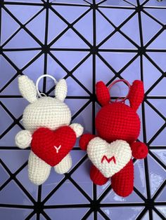 two crocheted red and white stuffed animals hanging on a black wire rack with purple background