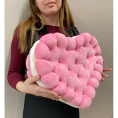 a woman holding a pink heart shaped pillow