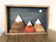 three mountains in a wooden frame on top of a wood floor with the moon and stars above them