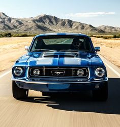 a blue muscle car driving down the road with mountains in the backgroup