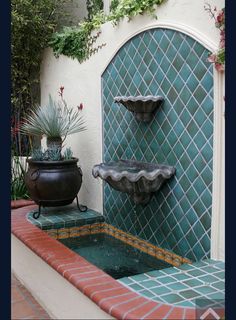 a water fountain in the middle of a courtyard with potted plants on either side