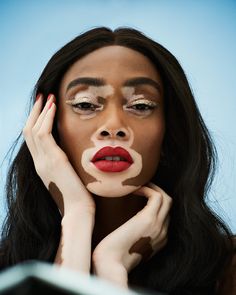 a woman with makeup painted on her face is looking at the camera and holding her hand to her cheek