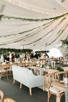 tables and chairs are set up in a tent with greenery hanging from the ceiling