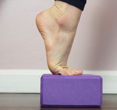 a person standing on top of a purple block with their feet up and one foot in the air