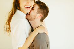 a man and woman embracing each other in front of a white wall with their arms around each other