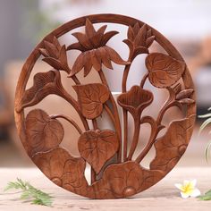 a wooden plate with flowers and leaves carved into the center, on a table next to a potted plant