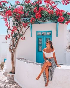 a woman sitting on the side of a building next to a tree with red flowers