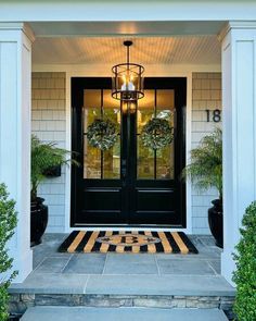 a black front door with two potted plants and a lantern hanging from the ceiling