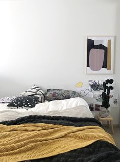 an unmade bed in a white room with black and yellow decor on the walls