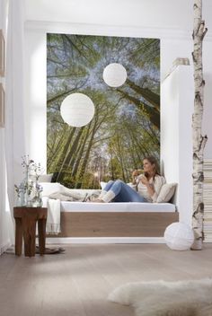 a woman sitting on top of a bed in a bedroom next to a tree filled forest