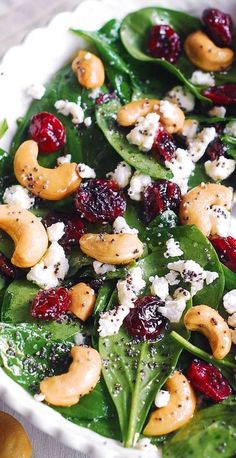 spinach salad with cranberries, nuts and feta cheese in a white bowl