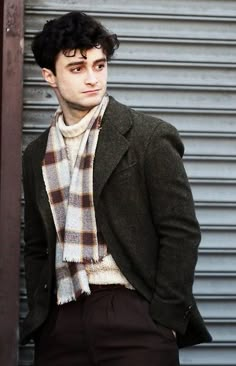 a man wearing a scarf standing next to a metal building with his hands in his pockets