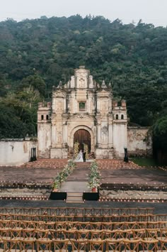 an outdoor wedding venue in front of a large building with trees on the hill behind it