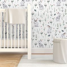 a baby's room with a white crib and wallpaper that has rabbits on it