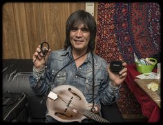 a man sitting on a couch holding up a cell phone and an instrument in front of him