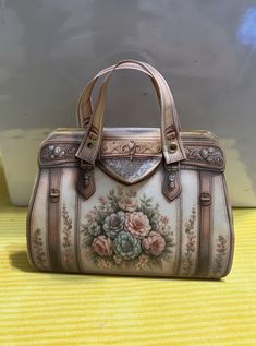 a handbag with flowers painted on it sitting on a yellow tableclothed surface