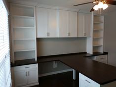 an empty kitchen with white cabinets and black counter tops in front of a ceiling fan