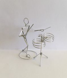 a metal figure holding scissors on top of a wire stand next to a white wall