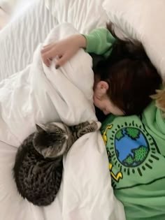 a little boy laying in bed with two cats sleeping on top of him and under the covers