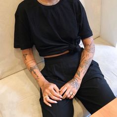 a person sitting on a couch with tattoos on their arms and legs, wearing a black shirt