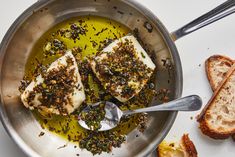 two pieces of fish sitting in a pan with bread and olive oil on the side