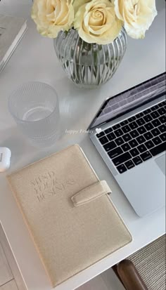 an open laptop computer sitting on top of a desk next to a vase with flowers