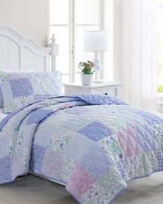 a white bed topped with a blue and pink quilted bedspread next to a window