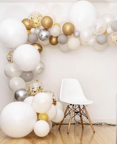 white and gold balloons are hanging in the corner of a room, with a chair next to it