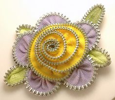 a yellow and purple flower brooch with green leaves on the side, sitting on a white surface