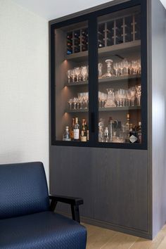 a glass cabinet with wine glasses and liquor bottles in it is next to a blue chair