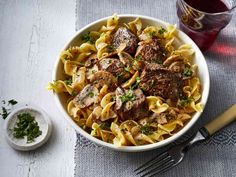 a white bowl filled with pasta and meat on top of a table next to a fork