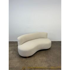 a curved white couch sitting on top of a cement floor